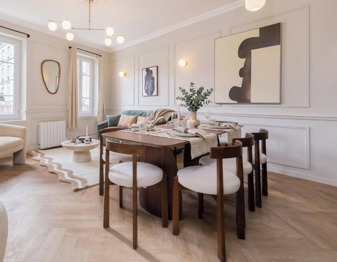 A dining area with a round table, wooden chairs, and a sofa in the background.