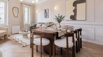 A dining area with a round table, wooden chairs, and a sofa in the background.