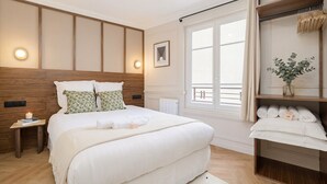 Un dormitorio con una cama grande, mesitas de noche, una ventana con cortinas, un radiador y un estante con toallas.