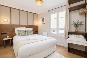 Un dormitorio con una cama grande, mesitas de noche, una ventana con cortinas, un radiador y un estante con toallas.
