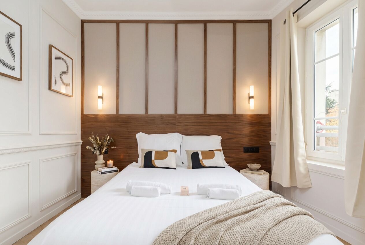A hotel room with a large bed, bedside tables, wall-mounted lights, and a window with curtains.