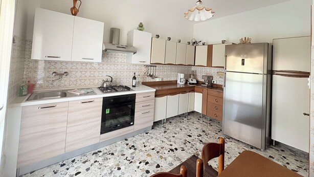 A kitchen with white cabinets, a stainless steel refrigerator, a gas stove, and a coffee maker.