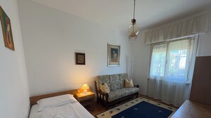 A room with a bed, a sofa, a rug with animal prints, a hanging light fixture, and a window with curtains.