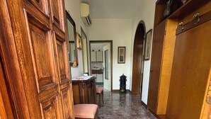 A hallway with a wooden door, a bench, a tiled floor, and a cabinet with decorative items.