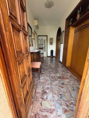 A hallway with a wooden door, a bench, a tiled floor, and a cabinet with decorative items.