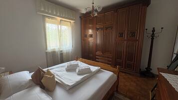 A bedroom with a bed, a wardrobe, a window with curtains, and a floor lamp.