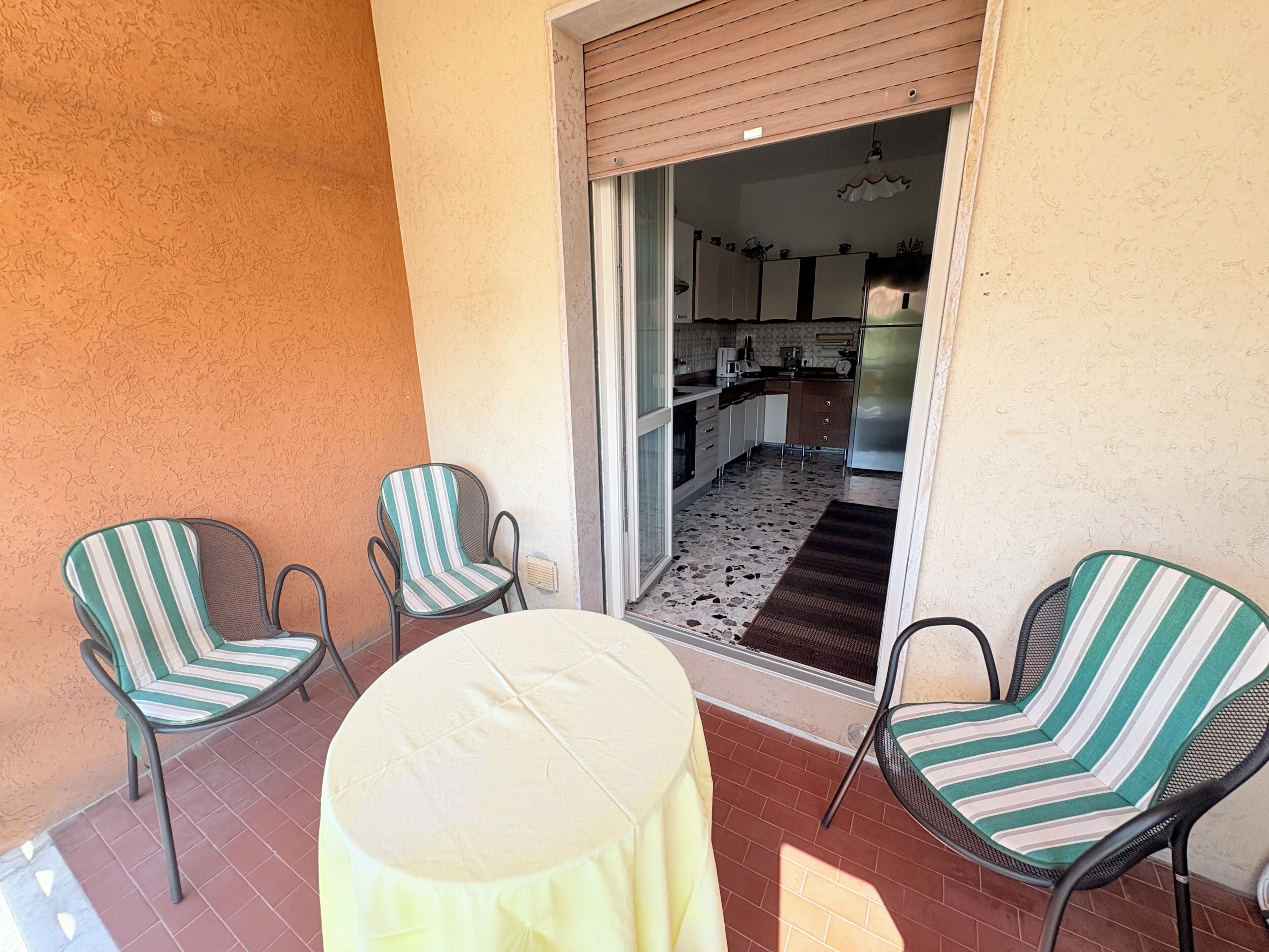 Une terrasse avec deux chaises à rayures et une table ronde, qui donne sur un espace cuisine équipé d’un réfrigérateur et de placards.