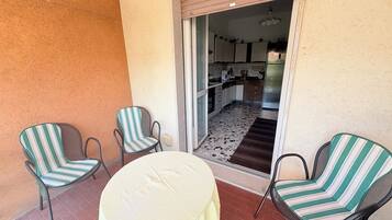 A patio with two striped chairs and a round table, leading to a kitchen area with a refrigerator and cabinets.