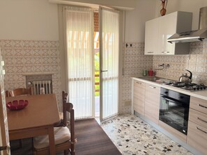 A kitchen with a dining table, chairs, a stove, oven, and a window with curtains.