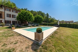 Una piscina rectangular amb un solàrium revestit de rajoles, envoltada per un prat i un setal.