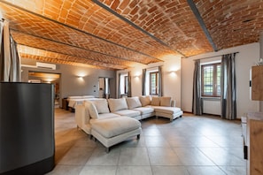 A spacious living area with a brick ceiling, large windows, and a sectional sofa. - Exclusive Villa with Swimming Pool and Tennis Area (Frinco)