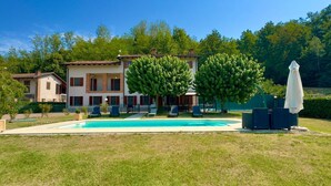 A two-story house with a swimming pool, outdoor seating, and a large tree in the front yard.