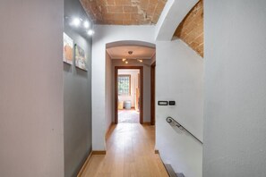 A hallway with a wooden floor, white walls, and a brick ceiling. There is a door on the right with a metal handle and a light switch above it. - Exclusive Villa with Swimming Pool and Tennis Area (Frinco)