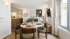 Un comedor con una mesa redonda dispuesta para cuatro personas, rodeada de sillas de madera con tapicería verde.