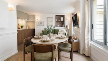 A dining area with a round table set for four, surrounded by wooden chairs with green upholstery.
