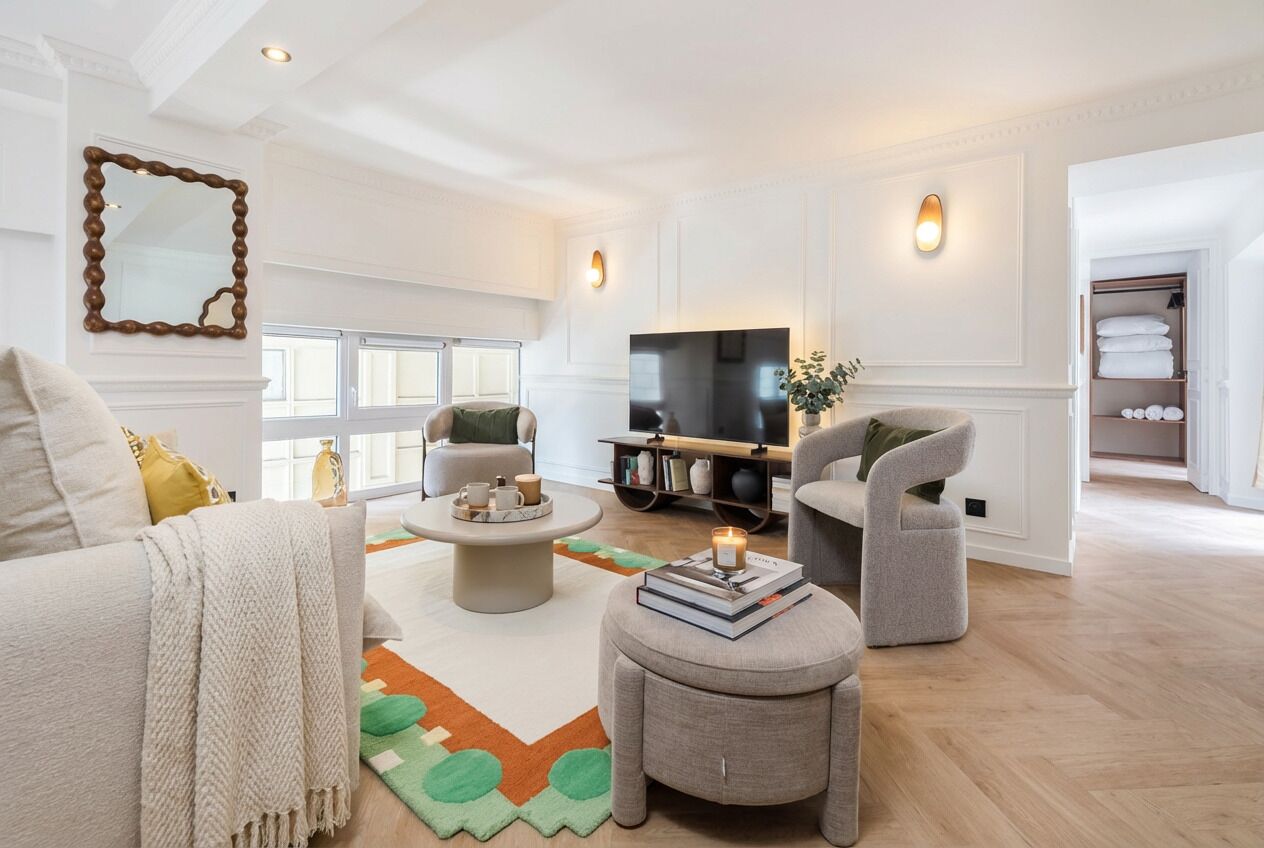 Een woonkamer met een bank, fauteuils, een salontafel en een televisie. Er is een boekenkast en een spiegel aan de muur.