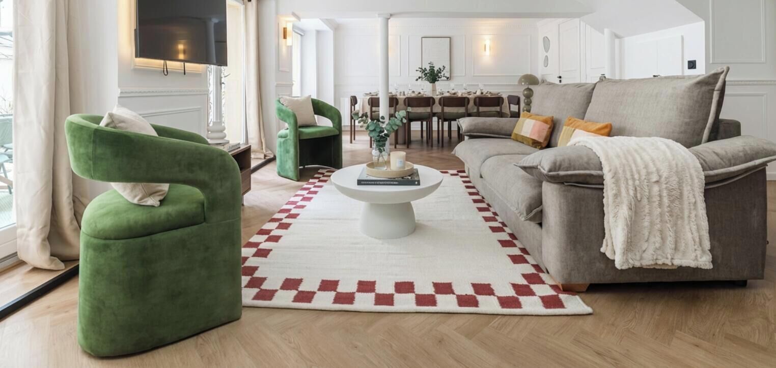 A modern living room with a sofa, armchairs, a coffee table, and a dining area in the background.