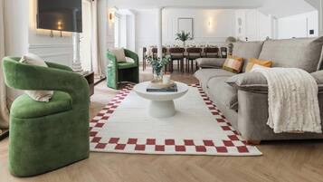 A modern living room with a sofa, armchairs, a coffee table, and a dining area in the background.