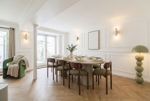A dining area with a round table set for six, surrounded by chairs, with a green armchair and a floor lamp in the foreground.