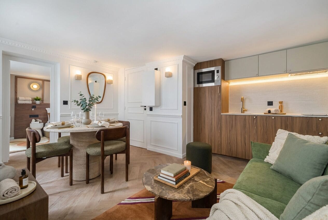 Una sala de estar moderna con un sofá verde, un comedor con una mesa redonda y una cocina con armarios de madera y un microondas.