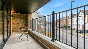 Un balcon donnant sur une rue résidentielle, avec une rambarde en métal et un banc en bois.