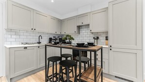 A modern kitchen with white cabinetry, a central island with stools, and a tiled backsplash. - Modern 1 Bedroom Stay Balcony East Croydon (Croydon)