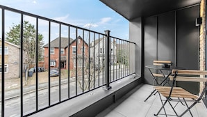A balcony with a metal railing, a table with chairs, and a view of a residential street. - Modern 1 Bedroom Stay Balcony East Croydon (Croydon)