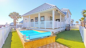 Ein zweistöckiges Haus mit einer überdachten Veranda, einem Schwimmbad und einem eingezäunten Garten.