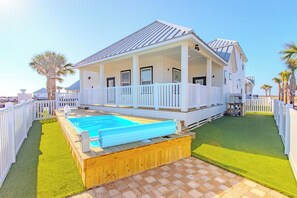 Ein zweistöckiges Haus mit einer überdachten Veranda, einem Schwimmbad und einem eingezäunten Garten.