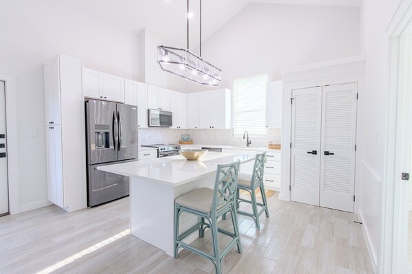 A modern kitchen with white cabinetry, stainless steel appliances, a central island, and a dining area with chairs.