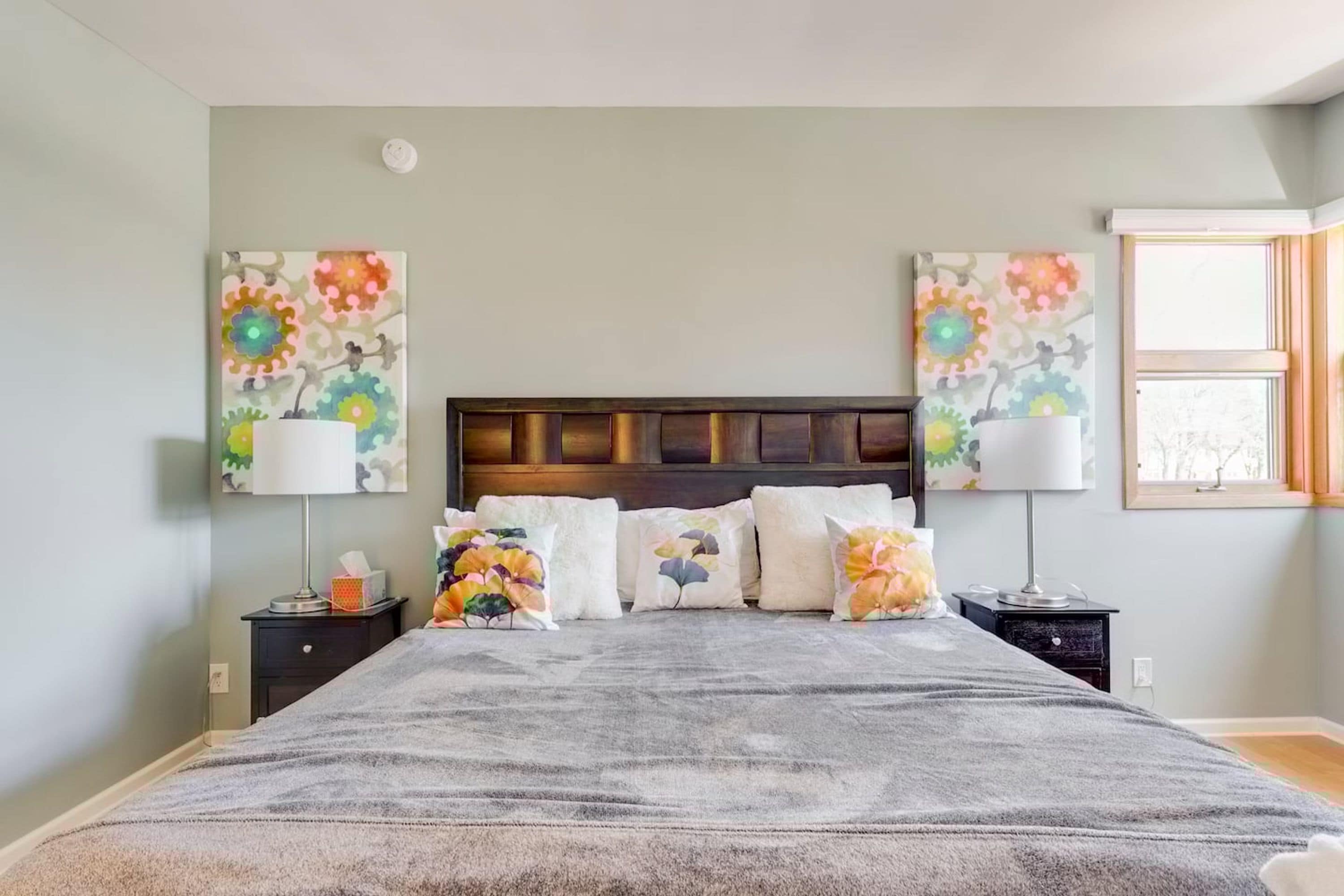 A bedroom with a bed, two nightstands, a window, and floral wall art.