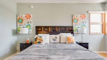 A bedroom with a bed, two nightstands, a window, and floral wall art.