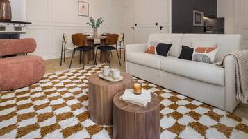 Uma sala de estar com um sofá branco, uma poltrona rosa, uma mesa de centro de madeira e um tapete estampado.