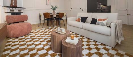 Un salon avec un canapé blanc, un fauteuil rose, une table basse en bois et un tapis à motifs.