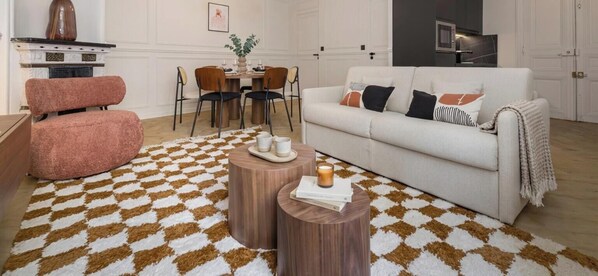 Una sala de estar con un sofá blanco, un sillón rosa, una mesa de centro de madera y una alfombra estampada.