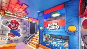 Quarto com tema Super Mario, incluindo cama com colcha temática do Mario, parede com mural do Mario e área de recreação com figuras do Mario e Luigi.