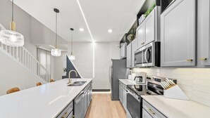 Uma cozinha moderna com uma ilha central, eletrodomésticos de aço inoxidável e iluminação pendente.