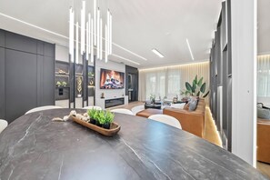 Un espace repas moderne avec une table en marbre foncé, un plateau de service en bois agrémenté de plantes et un grand téléviseur à écran plat fixé au mur.