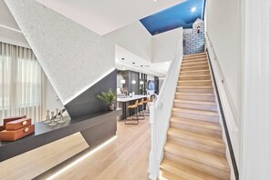Una cocina moderna con una isla central, una escalera de madera y una zona de comedor con taburetes de bar.