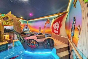 Una habitación con una cama grande con forma de barco, un pequeño escenario con un telón de fondo y una pared con un diseño de calavera.
