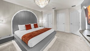 Quarto moderno com cabeceira curva, cama grande, lustre e televisão de tela plana.