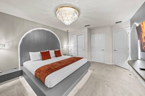 Ein modernes Schlafzimmer mit einem gebogenen Kopfteil, einem großen Bett, einer Kristallleuchtre und einem Flachbildfernseher.
