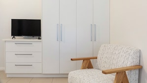 A room with a white wardrobe, a television on a white cabinet, and a patterned armchair.