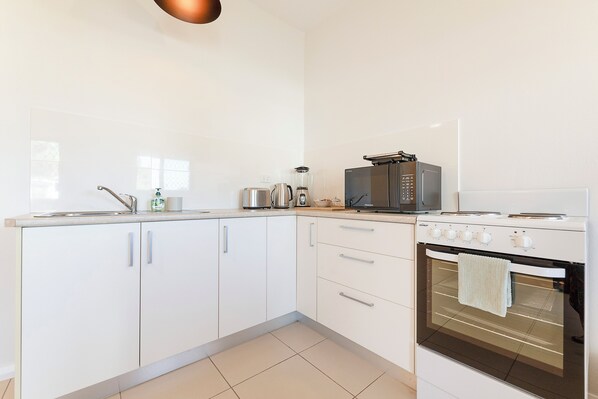 A modern kitchen with white cabinets, a stainless steel stove, a microwave, and a kettle.