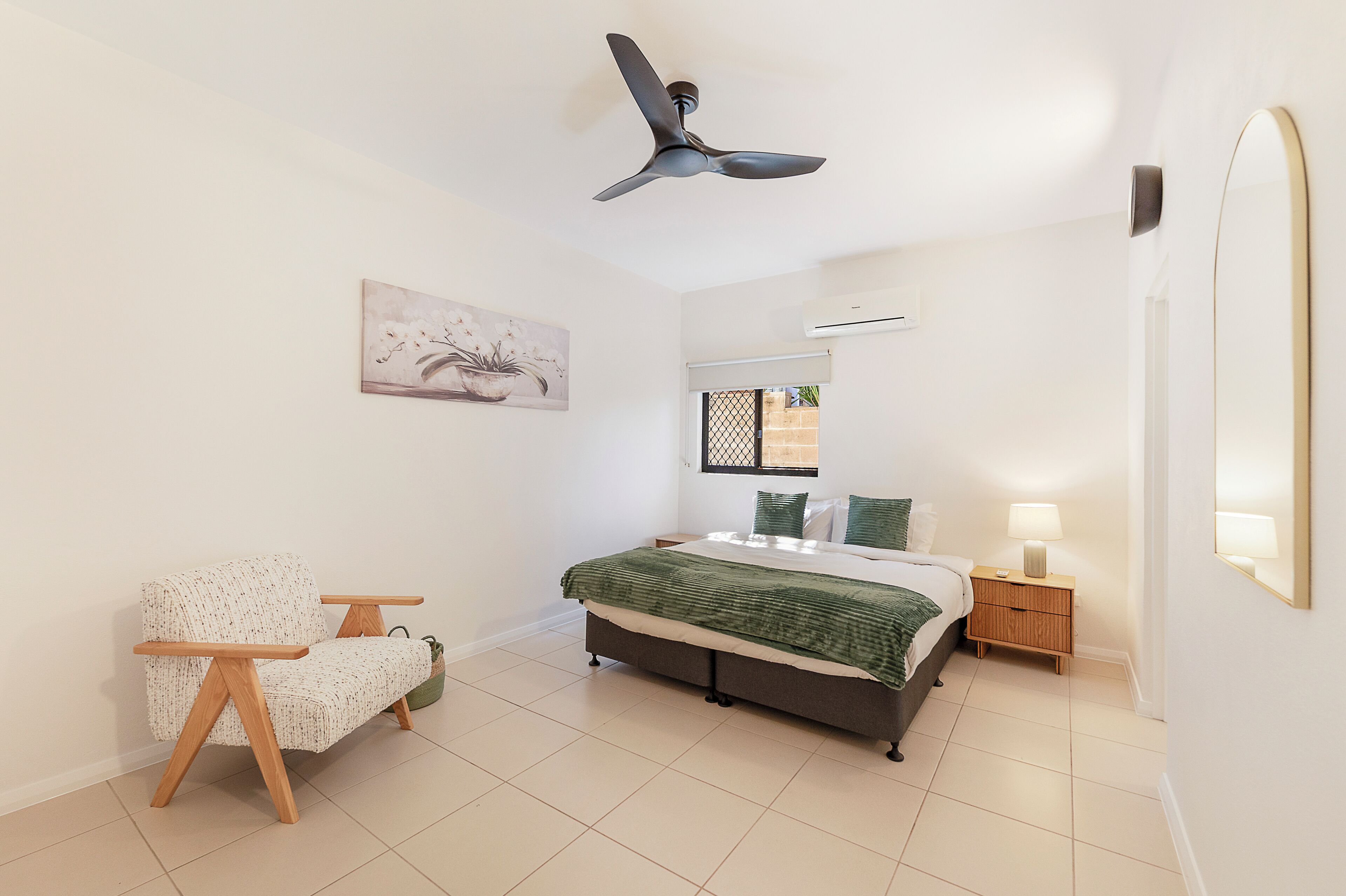 A bedroom with a bed, a chair, a nightstand, an air conditioning unit, a window, and a ceiling fan.