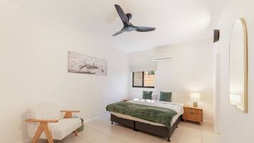 A bedroom with a bed, a chair, a nightstand, an air conditioning unit, a window, and a ceiling fan.