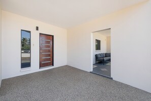 A hallway with a wooden door and a window, leading to a seating area with a sofa.