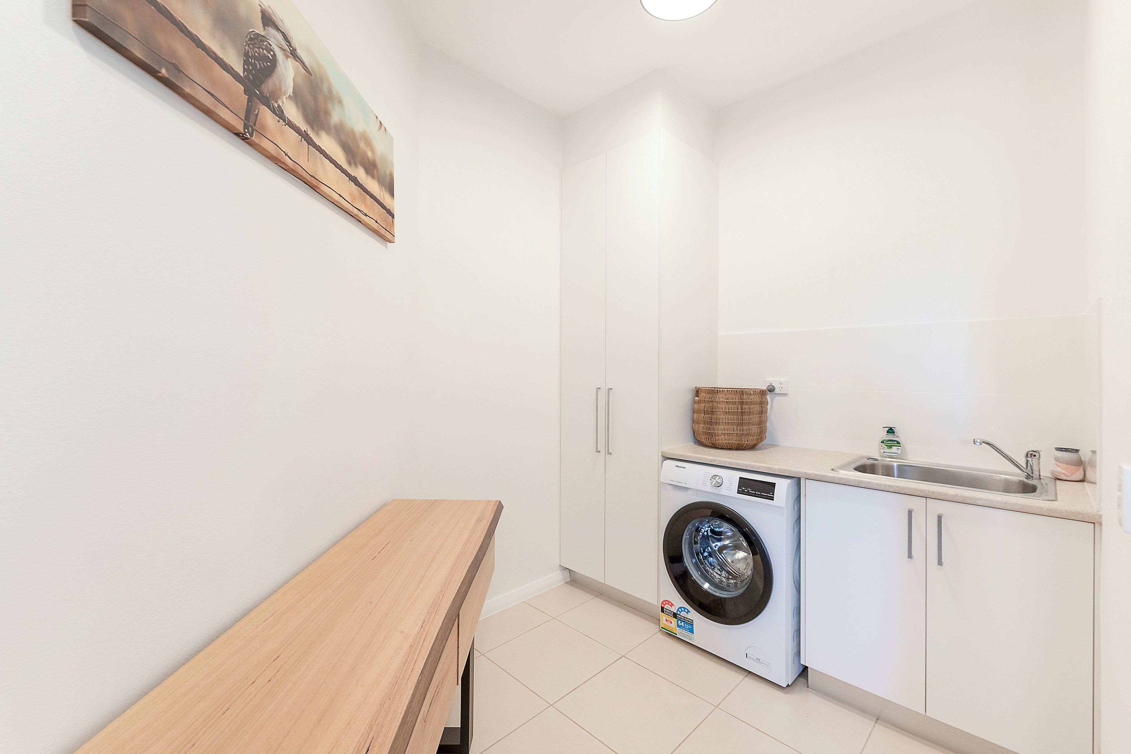 A laundry room with a washing machine, a sink, and a wooden bench.