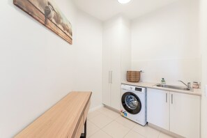 A laundry room with a washing machine, a sink, and a wooden bench.