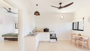 A modern kitchen with white cabinetry, a central island, a dining area with a wooden table and chairs, and two ceiling fans.
